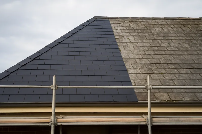 A hipped roof half re-slated, new dark slate beside weathered slate, scaffold at the eave — slate roof replacement, Ballarat. Illustrative example.